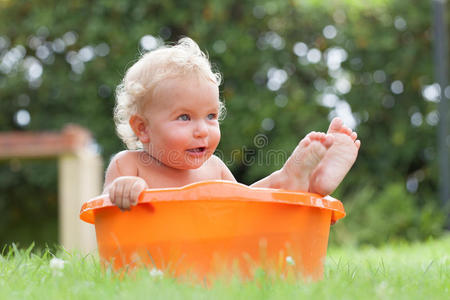 快乐可爱的卷发宝宝沐浴在橙色的骨盆里