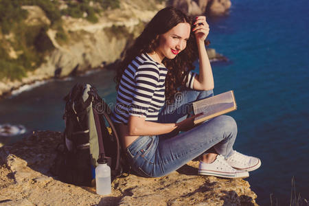 女孩旅行者坐在岩石峰上看书