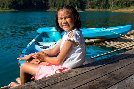 亚洲可爱的女孩坐在湖边的码头皮艇公园里。