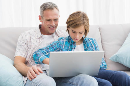 父亲和儿子坐在沙发上用笔记本电脑