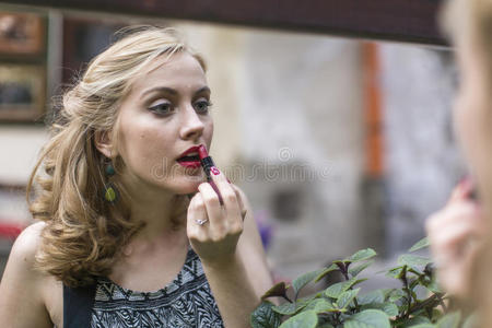 美丽的女人在镜子附近涂着口红。