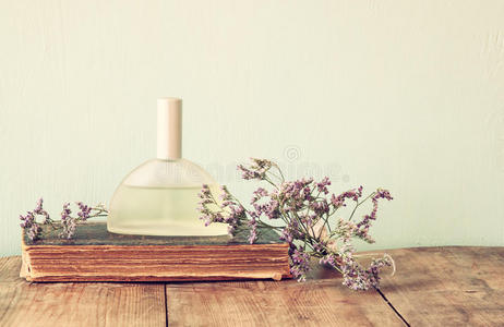 木制桌子上芳香花旁边的新鲜老式香水瓶。 复古过滤图像