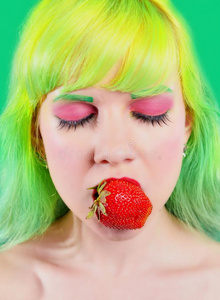 美丽的女孩与彩色头发持有草莓与嘴唇在绿色背景