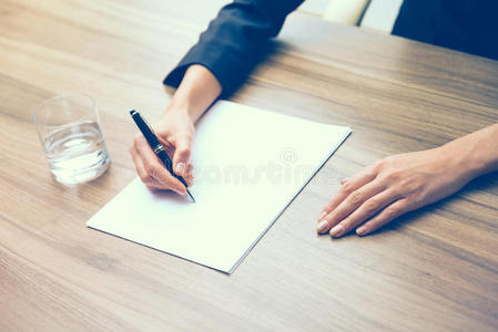 特写一个商业女人的手，同时写下一些基本的信息。 一杯水，纸和一支钢笔。