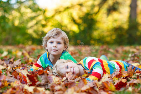 两个小男孩穿着五颜六色的衣服躺在秋叶里