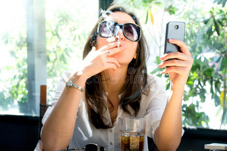 黑发女人抽烟,看着智能手机照片