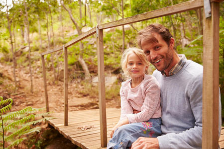 父亲和小女儿坐在森林里的一座桥上