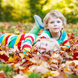 两个小男孩穿着五颜六色的衣服躺在秋叶里