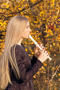 美丽的金发女郎在秋天的森林里吹长笛