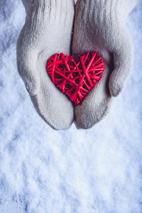 女性的手在白色针织手套与缠绕的复古浪漫红心在雪的背景。 爱和圣瓦伦丁的概念。