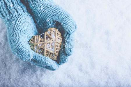 女性的手在一场白色的雪上，用浅茶色针织手套缠绕着米黄色的亚麻心。 爱，圣瓦伦廷斯日概念