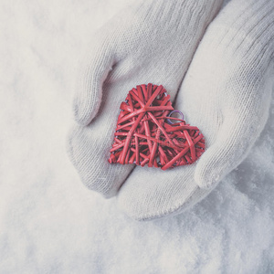 女性的手穿着白色针织手套，在雪地上有一颗交织的复古浪漫的红心。 爱和圣瓦伦丁的概念。