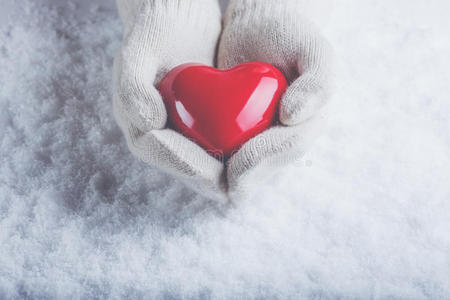 白色雪花红色手套女性的手在白色针织手套与光泽红色的心在雪的背景.