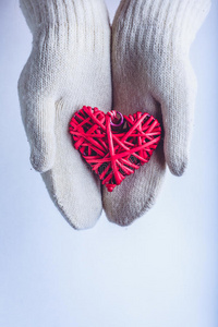 女性的手在白色针织手套与缠绕的复古浪漫红心在雪的背景。 爱和圣瓦伦丁的概念