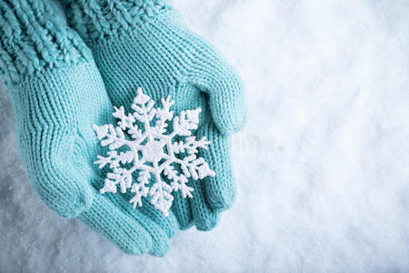 女性的手在白色的雪背景上，白色的泰尔针织手套与闪闪发光的美妙雪花。 冬天，圣诞节的概念