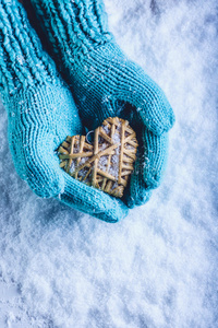 女性的手在白色的雪背景上，用浅色针织手套与缠绕的米色亚麻心。 圣情人节概念