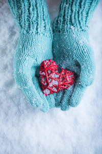 女性的手在泰尔针织手套与缠绕的复古浪漫的心在雪的背景。 爱和圣瓦伦丁的概念