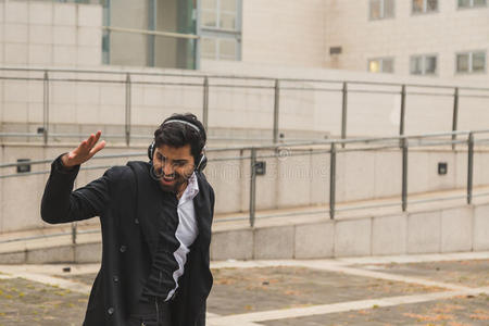 英俊的印度男人在城市背景下听音乐