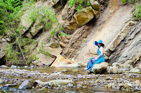 美丽的年轻女孩坐在河里的一块岩石上