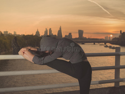 健身妇女在日出时在桥上伸展腿