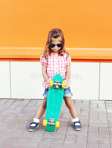 时尚的小女孩，滑板，戴太阳镜和格子衬衫在城市