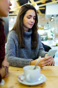 美丽的年轻女人在咖啡店用手机。