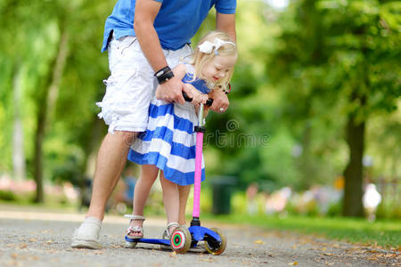 父亲教他的小女儿如何骑滑板车
