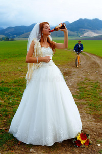 新娘带着啤酒瓶和新郎骑着自行车在背景上婚礼的概念。