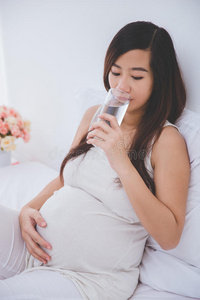 美丽的亚洲孕妇拿着一杯水，微笑着