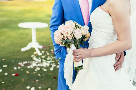 新娘带着一束粉红色的花，新郎穿着蓝色的西装，一起参加婚礼
