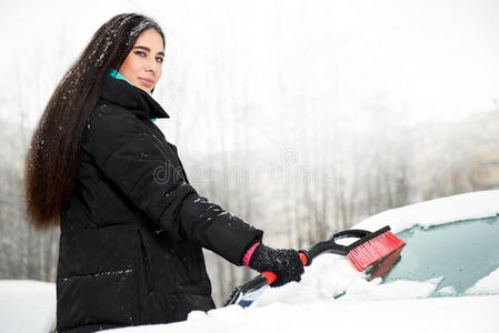 美丽的年轻有趣的女人把雪从她的车里移走