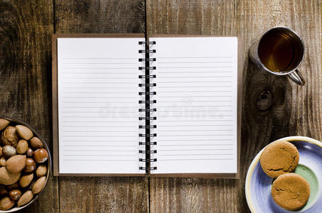 一本打开的笔记本，木桌上有空白页。一杯茶，坚果