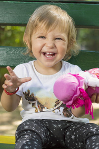 可爱的一岁女婴坐在长凳上，带着一个洋娃娃