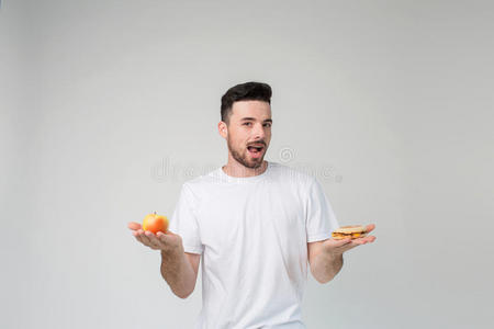 留胡子的人穿着白色衬衫，背景很轻，拿着一个汉堡包和一个苹果