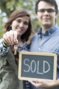 一对夫妇在新家前拿着出售的黑板标志和钥匙