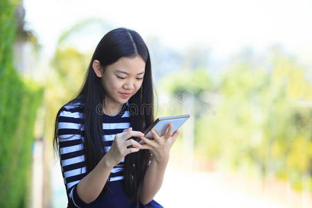 亚洲女孩和电脑平板电脑在手，用牙齿笑脸站立，用于人与互联网的连接交流