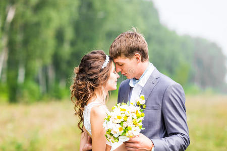 美丽的新娘和新郎站在草地上接吻。 新婚夫妇
