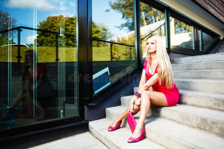 穿着粉红色连衣裙的金发年轻女子在现代建筑附近摆姿势
