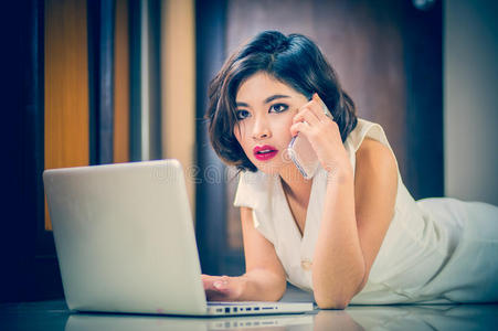 亚洲妇女使用智能手机和笔记本电脑躺在地板上