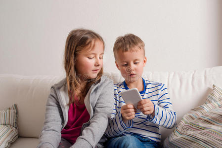 孩子们在家坐在沙发上，玩智能手机