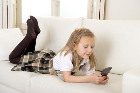 女孩子金发躺在家里的沙发上，使用手机上的互联网应用程序