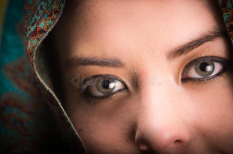 特写女性戴着蓝色灰色和棕色围巾，遮住头部，只露出美丽的绿色眼睛
