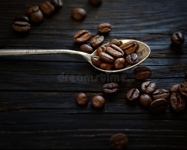 在深色木制背景上的金属勺子里的咖啡豆