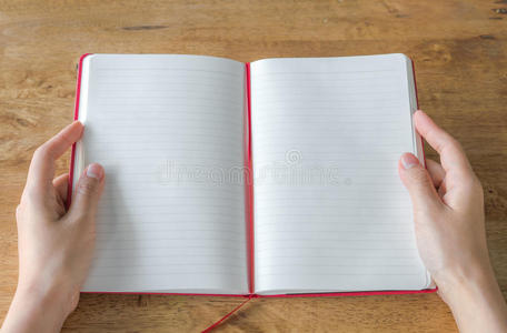 穿着蓝色夹克的女商人手里拿着一本红色的日记本.看着空白页思考.