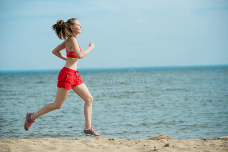 在阳光明媚的夏日沙滩上奔跑的年轻女士。训练。慢跑