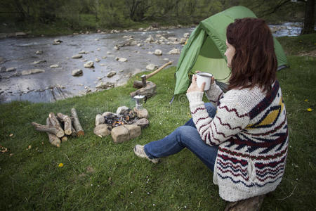 女孩坐在营地旁的女孩看着地图喝咖啡。