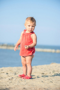 穿着红色连衣裙的女婴在海边的沙滩上玩耍。