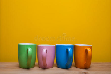 黄色背景的木桌上五颜六色的咖啡杯