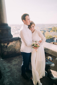 美丽的新婚夫妇拥抱阳台与城市景观背景