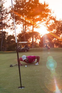 高尔夫球手在洞中吹球，背景为日落